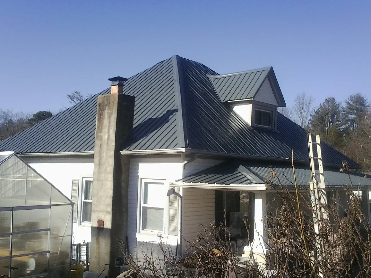 Dark blue standing seam metal roof on a white farmhouse with dormer — Slate & Tile Roof Repair by Roofing Brothers in New Vienna