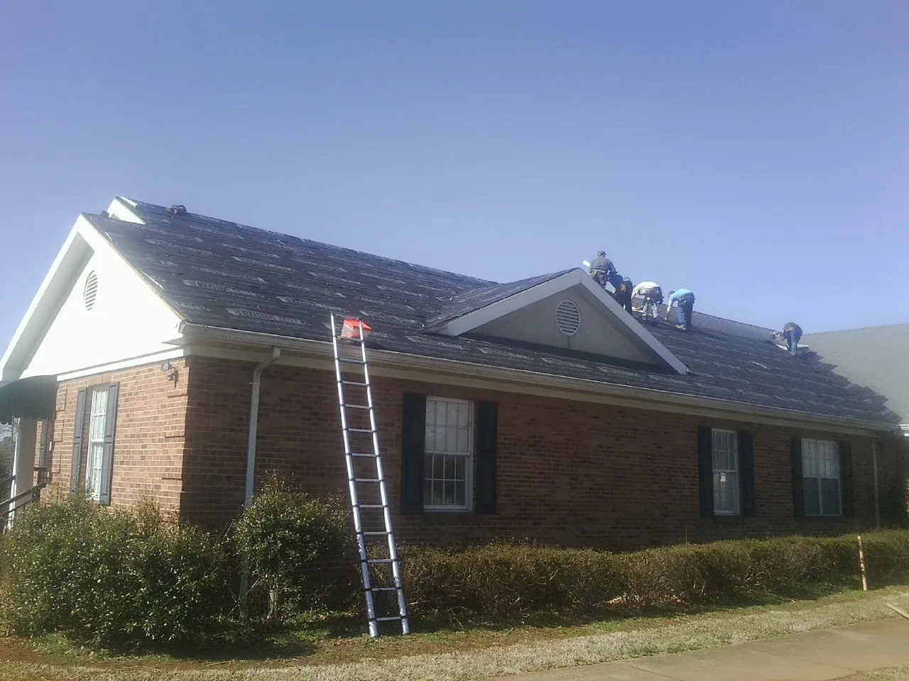 Crew tearing shingles off a brick ranch roof with a ladder set — Emergency Roof Repair work by our crew in New Vienna