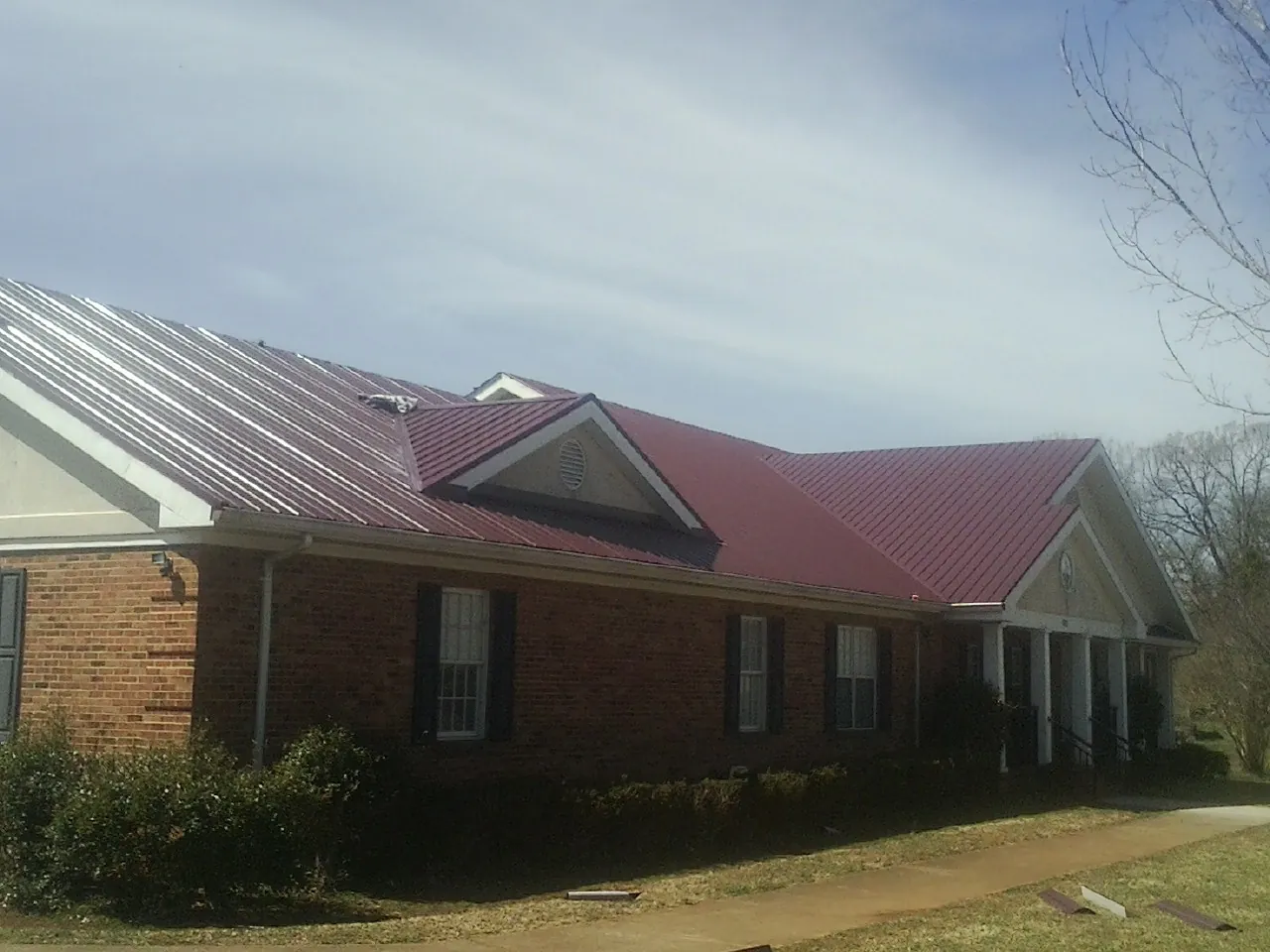 Red metal roof with gabled entries on a long brick building, from a Hail Damage Roof Repair job in New Vienna