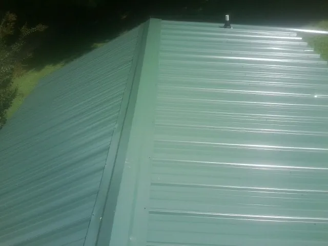 New green metal panels meeting at the ridge of a roof — Flat Roof Repair work by our crew in New Vienna